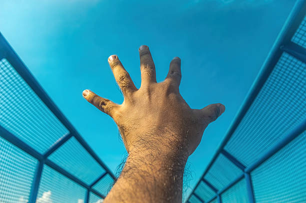 istock A human hand reaches dynamically upwards toward a vast, clear blue sky, framed by modern blue mesh architecture. Symbolizes aspiration, freedom, and reaching for limitless potential 2220880674