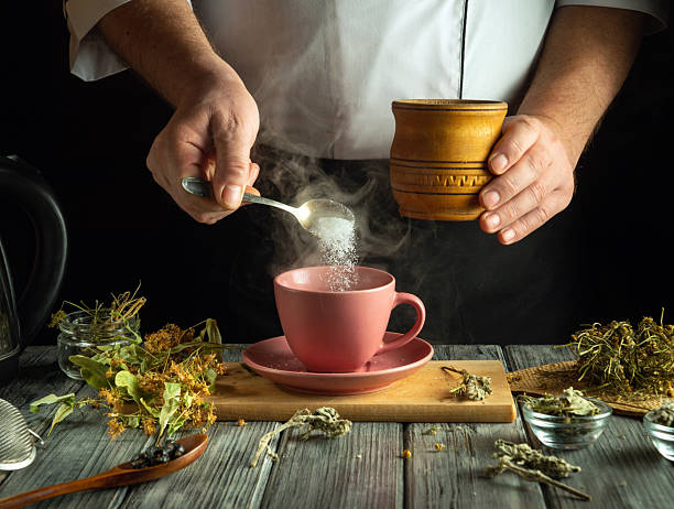 istock Hands skillfully blend dried herbs and sugar, creating a fragrant herbal drink in a warm kitchen. An inviting atmosphere, with natural elements surrounding a charming pink cup awaiting its infusion 2220880687