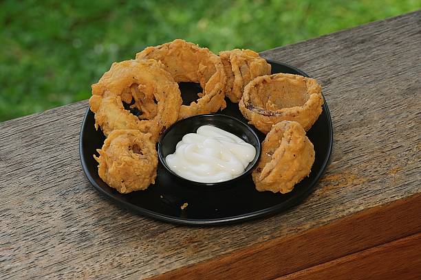 Delicious golden brown onion rings served with a white dipping sauce on a rustic wooden background. Perfect snack or appetizer for any occasion.