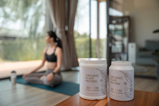 Whey protein containers in the foreground with a woman practicing yoga in the background, focusing on her breath and movement as part of her healthy lifestyle while also committing to fitness and nutrition
