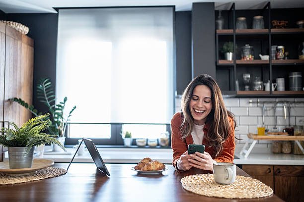 istock Smiling woman enjoying breakfast and using smartphone in modern kitchen 2220896865
