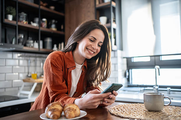 istock Young woman enjoying breakfast and using smartphone in modern kitchen 2220896927