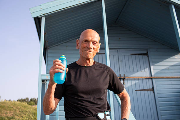 istock Positive active senior man with a water bottle by a beach hut 2220898488