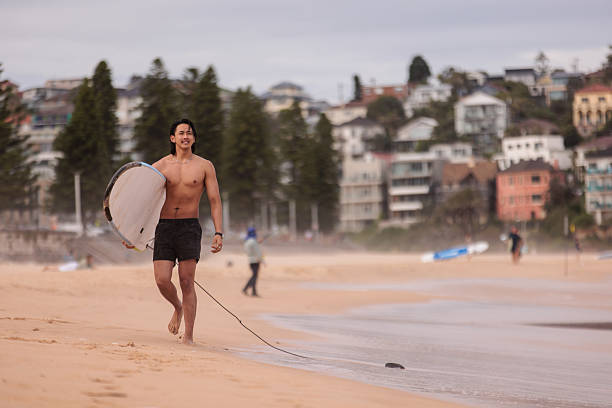 Athletic male surfer walks confidently along the shore after catching waves at Manly Beach.