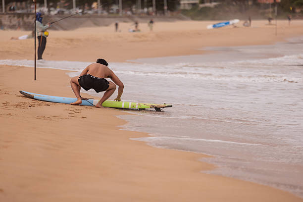 Young male surfer preparing his surfboard for a surf session at the Manly Beach.