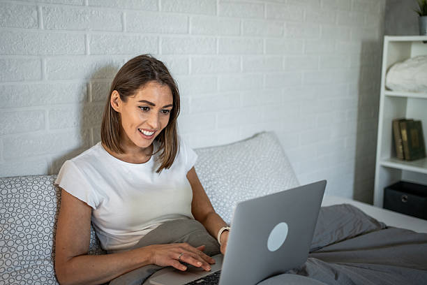 istock Young woman working remotely from her bed with laptop 2220902542