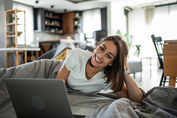 istock Young woman lying in bed is using laptop and smiling 2220903266