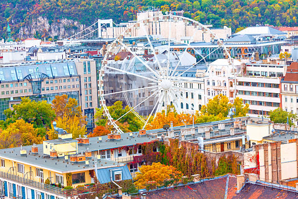 Colorful autumn view of Budapest featuring the Budapest Eye Ferris wheel surrounded by historic and modern buildings. Vibrant foliage and architectural variety create a lively and dynamic urban scene