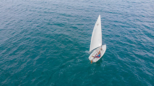 Three small boats (dinghys) are tied up to the dock. They are part of a sailing school, and are ready for a day on the water. Orange life preservers are stowed on board, and a breeze is ruffling the sails.