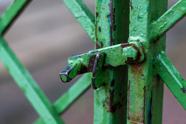 Close-up of weathered green metal gate with rusty latch and textured surface.