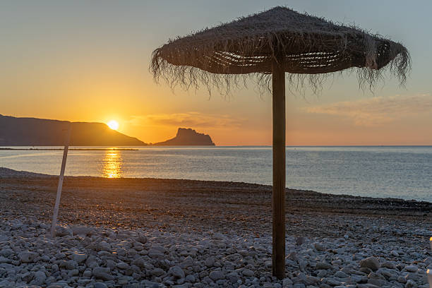 istock Straw parasol standing on a pebble beach at sunrise in Altea, Spain 2220911025