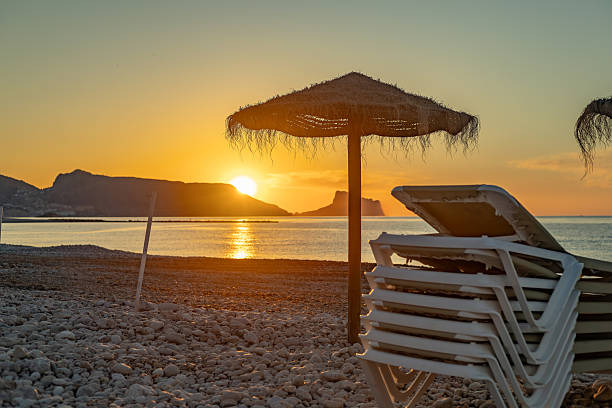 istock Sun rising over Altea beach with stacked deck chairs and parasol 2220911026