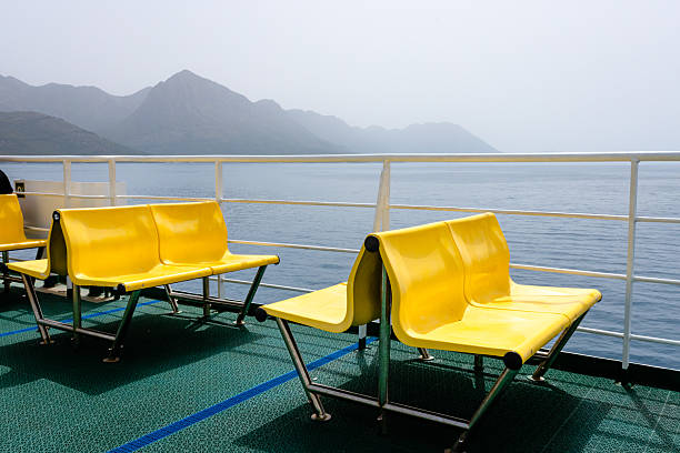 Vibrant yellow ferry seats on an open upper deck overlooking the calm Adriatic Sea and the dramatic coastline of Croatia. The image captures the peacefulness of maritime travel with a minimal yet bold visual contrast between the bright seating and the natural blues and greens of the sea and mountains. Perfect for conveying summer vacations, freedom, and slow travel.