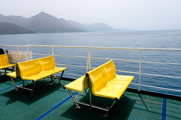 Vibrant yellow ferry seats on an open upper deck overlooking the calm Adriatic Sea and the dramatic coastline of Croatia. The image captures the peacefulness of maritime travel with a minimal yet bold visual contrast between the bright seating and the natural blues and greens of the sea and mountains. Perfect for conveying summer vacations, freedom, and slow travel.