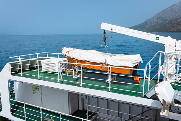 A brightly colored lifeboat rests securely on the upper deck of a Croatian ferry crossing the Adriatic Sea. Framed by a clear blue sky and distant mountainous coastline, this image evokes themes of safety, preparedness, marine transport, and Mediterranean travel. Ideal for editorial, infrastructure, and tourism stock collections.