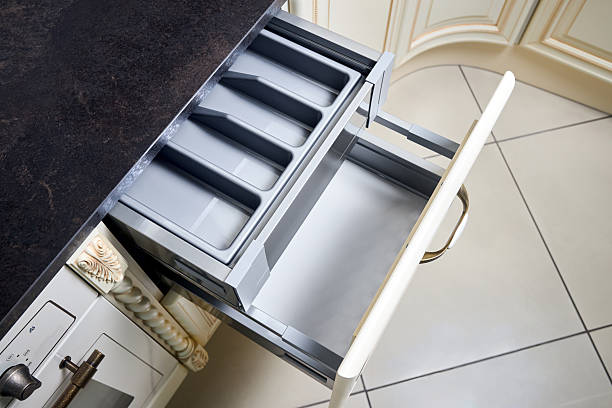 Solutions for placing utensils in classic kitchen - horizontal sliding pull out drawer shelves storage in a cupboard for kitchenware cookware under stoneware countertop white gas hob, with copy space.