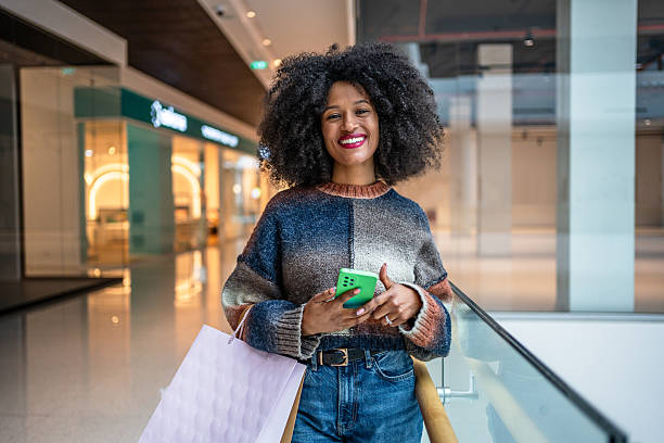 istock Smiling shopper using smartphone in mall holding shopping bags 2220927000