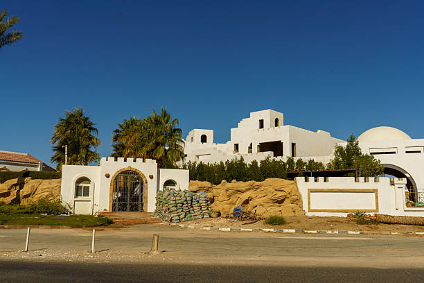 A large white house with a gate and a fence. The gate is open and there are some people standing near it