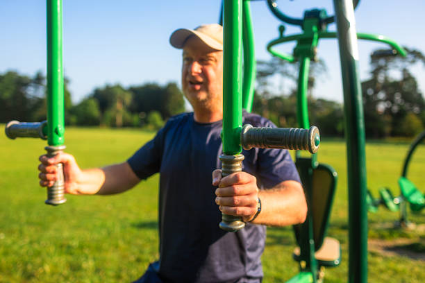 A mid adult male in his 40s uses the chest press at an outdoors gym in the park.