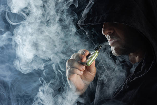 istock Mysterious Man Vaping in Hoodie with Dense Smoke Clouds, Modern E Cigarette Lifestyle Concept 2220933110