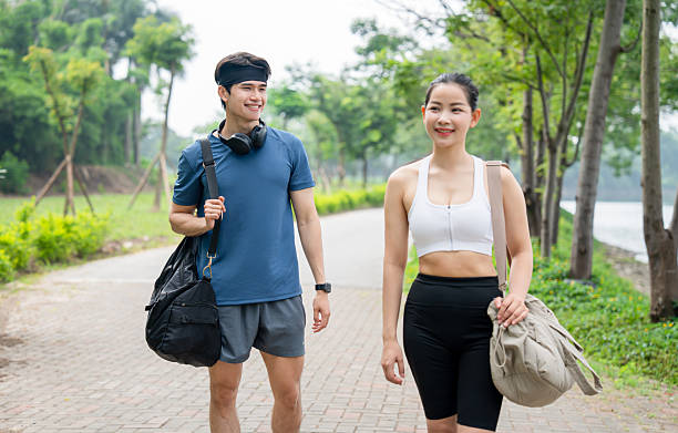 istock Athletic couple walks along a tree-lined path carrying their gym bags smiling and looking forward 2220933628