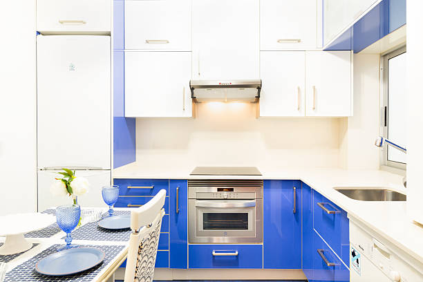 istock Wooden kitchen with white upper cabinets and blue lower cabinets, white wall, oven and white table 2220937640