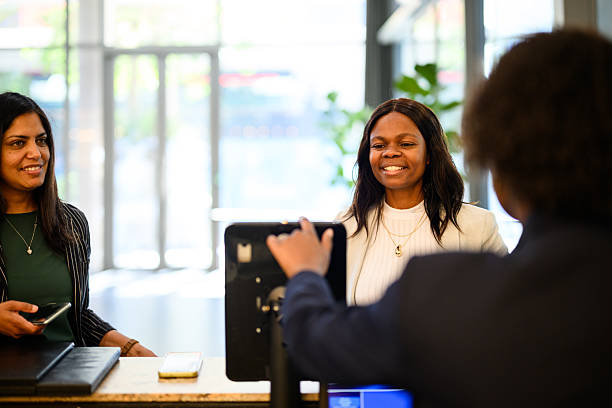 istock Two female hotel guests smiling while being assisted by a receptionist at the front desk, sunlit modern lobby in backdrop 2220940364