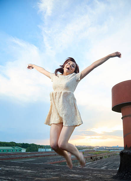 Beautiful young woman jumping with her hands up on the roof during summer sunset