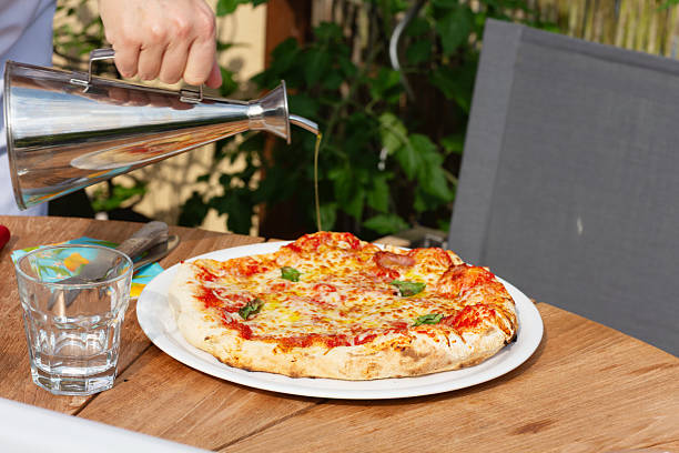 a plate with pizzza fresh from the oven, some olive oil is poutred over it, outdoors on patio