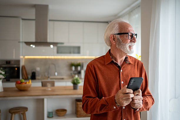 istock Senior man using smartphone and looking out the window in his modern kitchen 2220950718