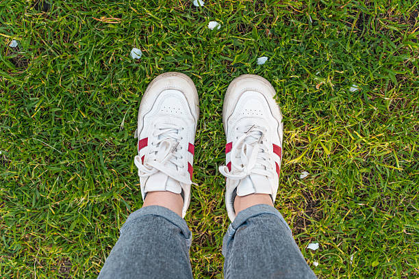 Women's feet in white sneakers on the grass, top view