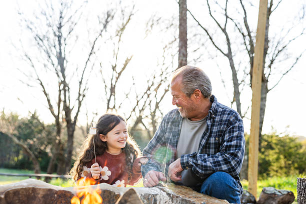 istock Grandfather and granddaughter roasting marshmallows by a bonfire 2220957968