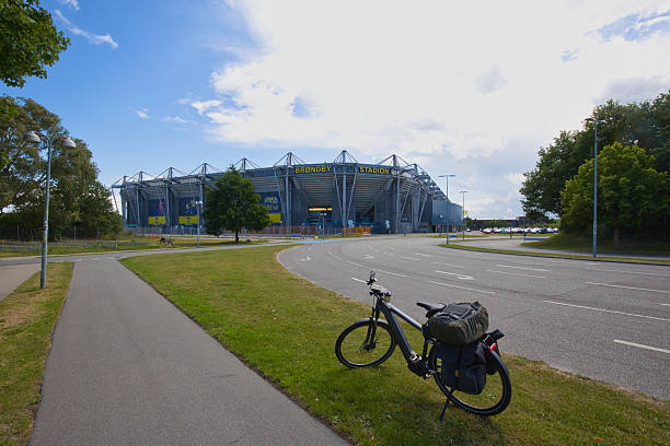 A packed e-bike stands on a grass strip next to the road in front of the Brøndby Stadium.