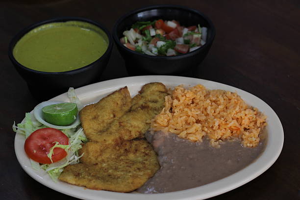 istock A vibrant presentation of a fried chicken plate accompanied by rice, beans, fresh salad, and green sauce, perfect for showcasing traditional cuisine in a culinary stock image. 2220961663