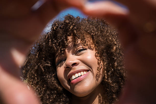 istock Young woman smiling framed by hands making heart shape 2220965231