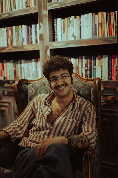 istock Young man smiling sitting in armchair in a library 2220973785