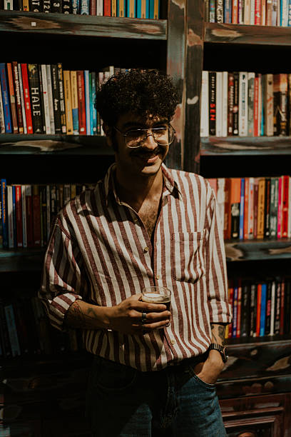 istock Young man smiling and holding a drink in a bookstore 2220975880
