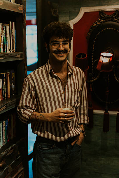 istock Young man smiling and holding a glass in a bookstore 2220975935