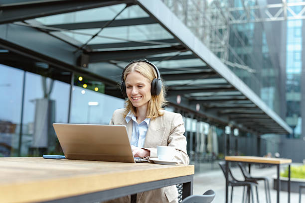 istock Woman wearing headphones using laptop outdoors at a coffee table 2220978183