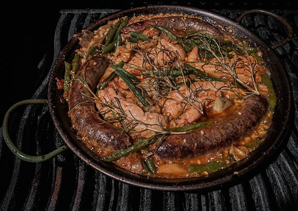 Paella with chicken, chorizo, green beans and artichokes prepared on a grill.