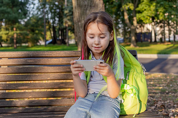 istock Young girl playing on smartphone outdoors in park on sunny day 2220992154
