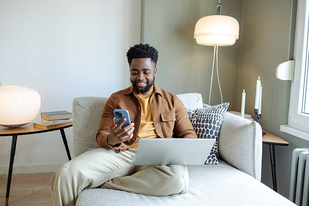 istock Man relaxing on couch while using smartphone and working on laptop at home 2220992864