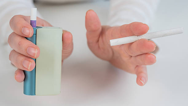 istock Woman holding regular and electronic cigarette on white background. Tobacco heating systems. 2220996329