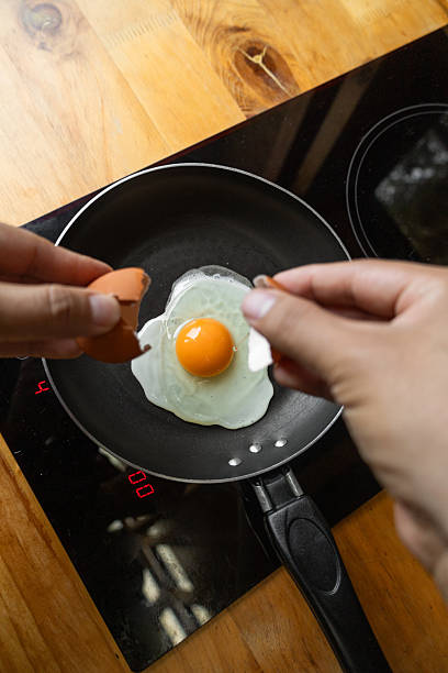 istock Hands cracking egg over black pan with egg frying inside, showing fresh cooking moment and warm kitchen scene 2221001733