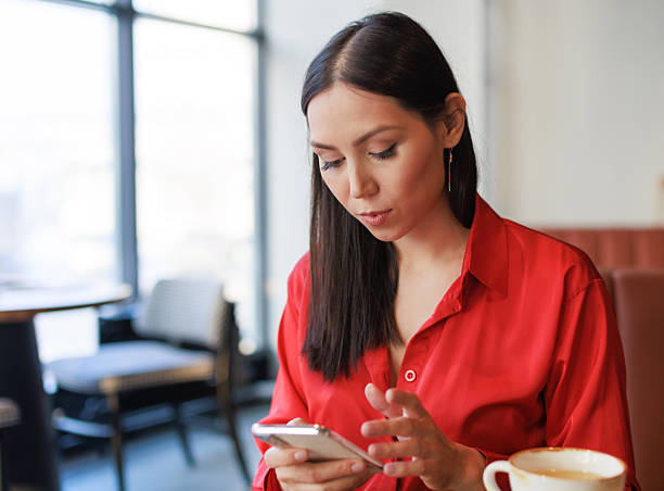 istock Smiling Asian Woman Using Smartphone While Relaxing in Modern Cafe 2221019487