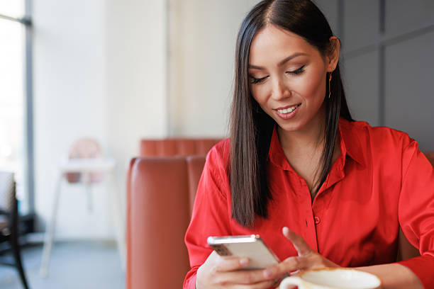 istock Smiling Asian Woman Using Smartphone While Relaxing in Modern Cafe 2221019494