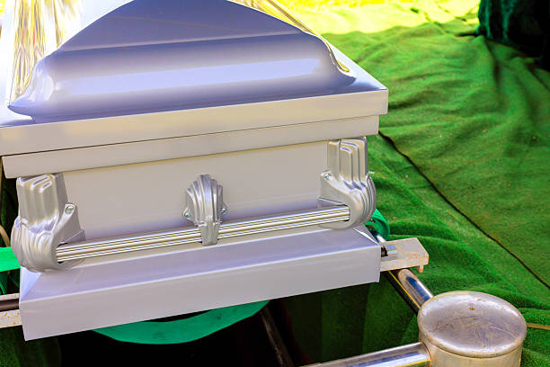 Silver coffin resting on a green burial cloth at a graveside service during the afternoon