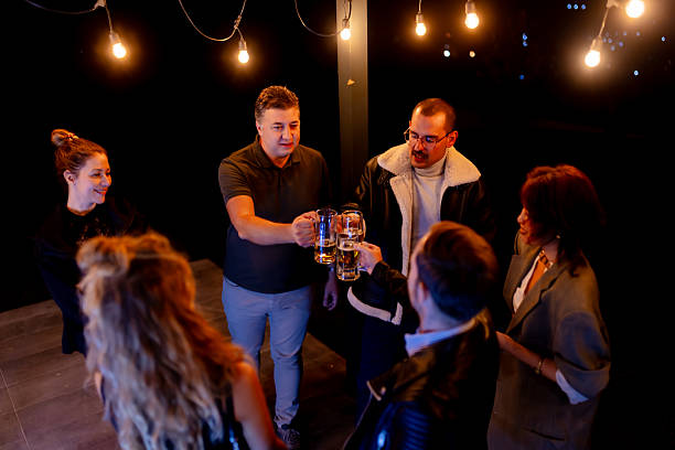 istock Group of Friends Celebrating Outside With Drinks Under Hanging Lights 2221023534