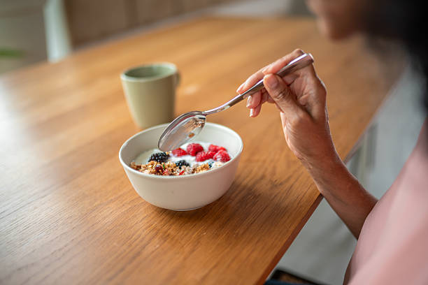 A senior Hispanic woman sits at a dining table, savoring a nutritious morning meal complete with fresh berries and cereal, reflecting a serene, healthy lifestyle.