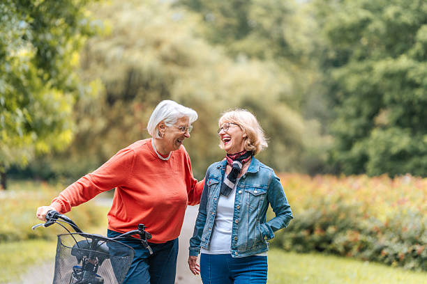 istock Senior Friends Stroll with Bicycle in Park 2221029556